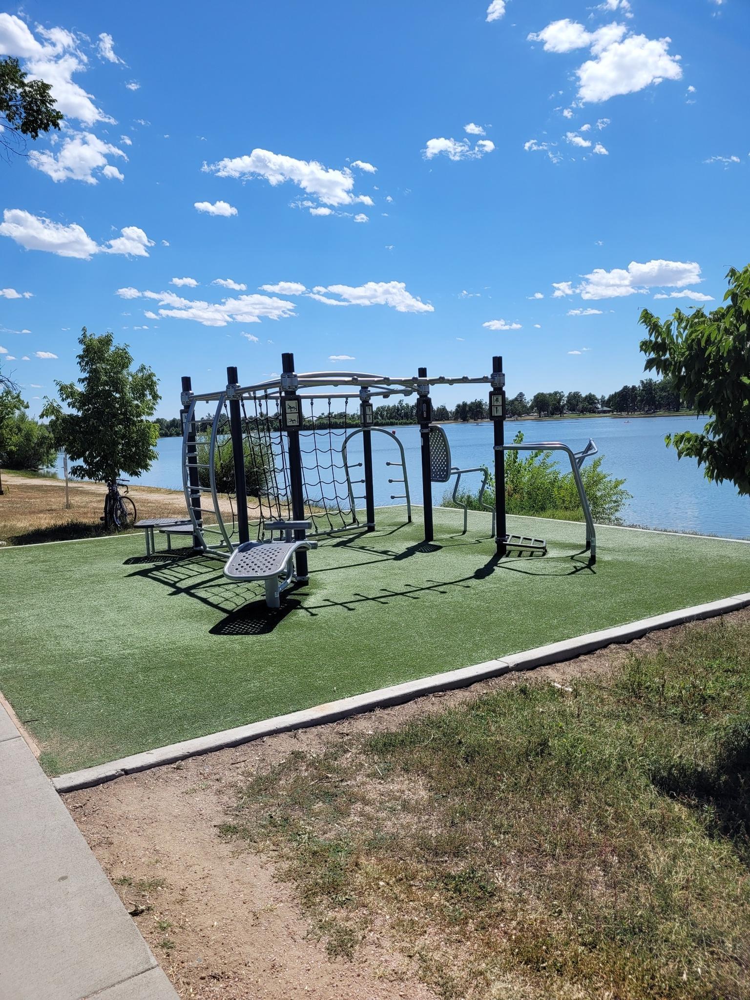 Sunny day with outdoor gym equipment beside a calm body of water.
