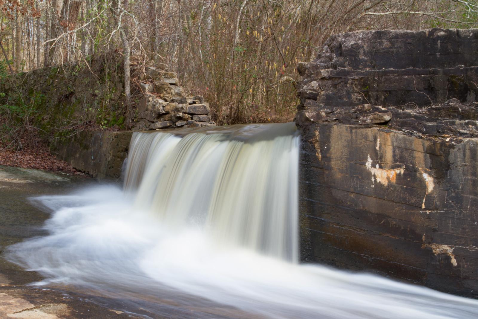Water cascades over a small man-made waterfall in a forest.
