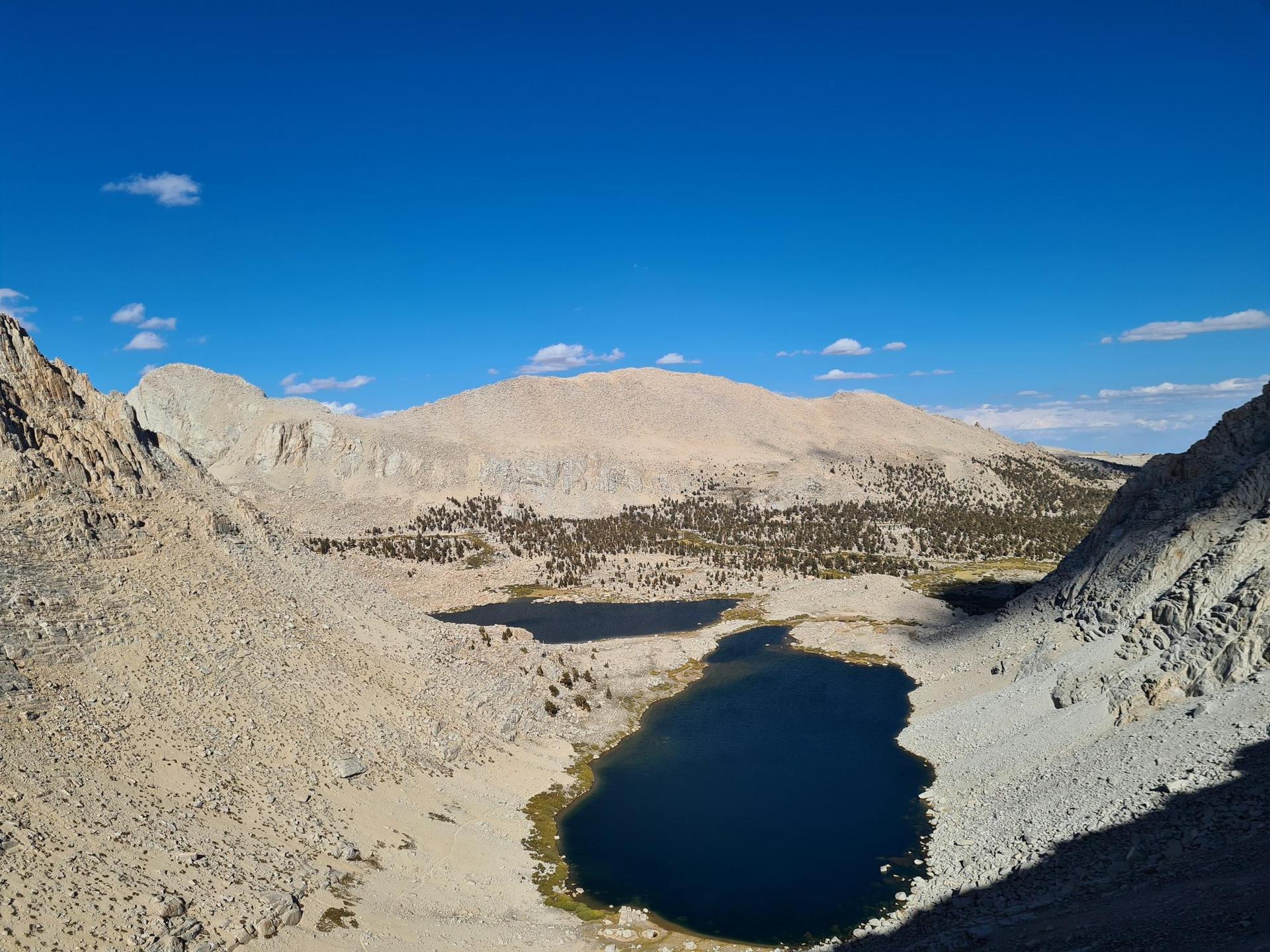 Two dark lakes in a rocky mountain valley under a clear blue sky.