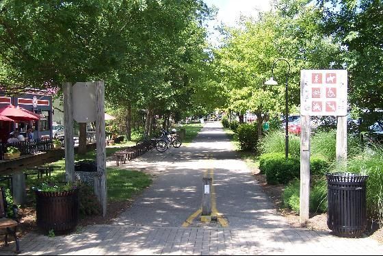 Sunny paved pathway lined with green trees, signs, and trash cans. - Little Miami Scenic Trail