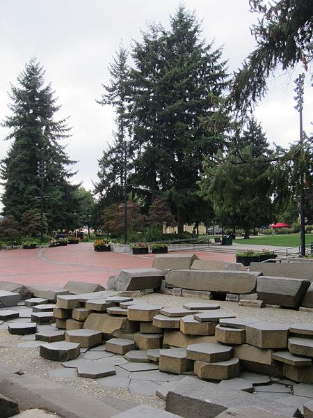 Stone blocks and tall evergreen trees in an overcast urban park setting.