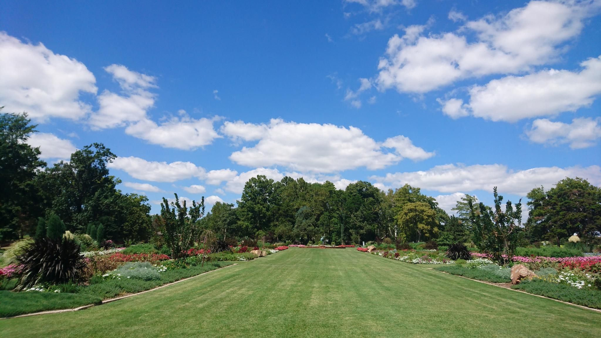 Wide green lawn surrounded by colorful gardens under a blue sky. - Will Rogers Trail