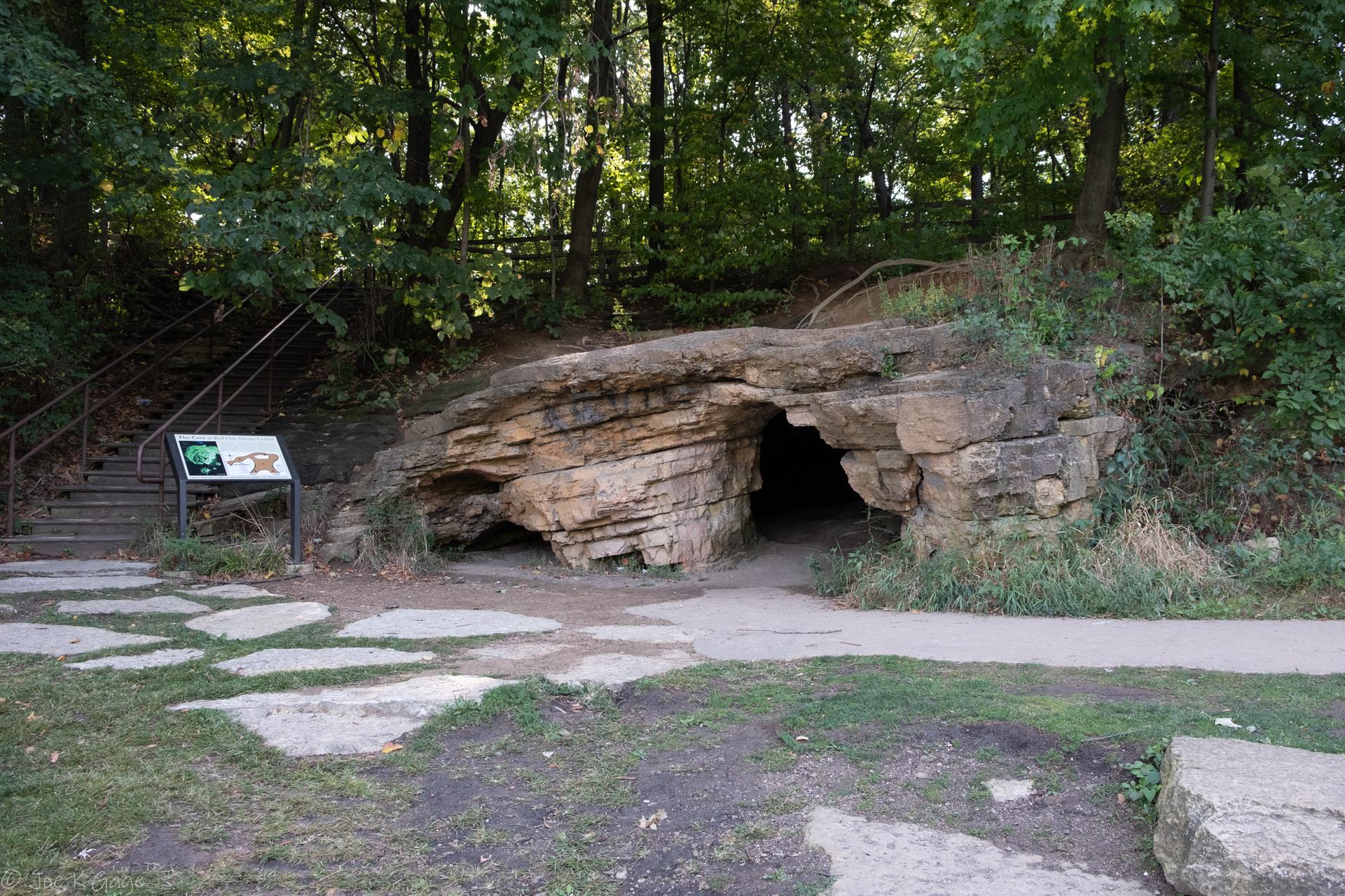 A large rock formation with a cave entrance next to a paved path.