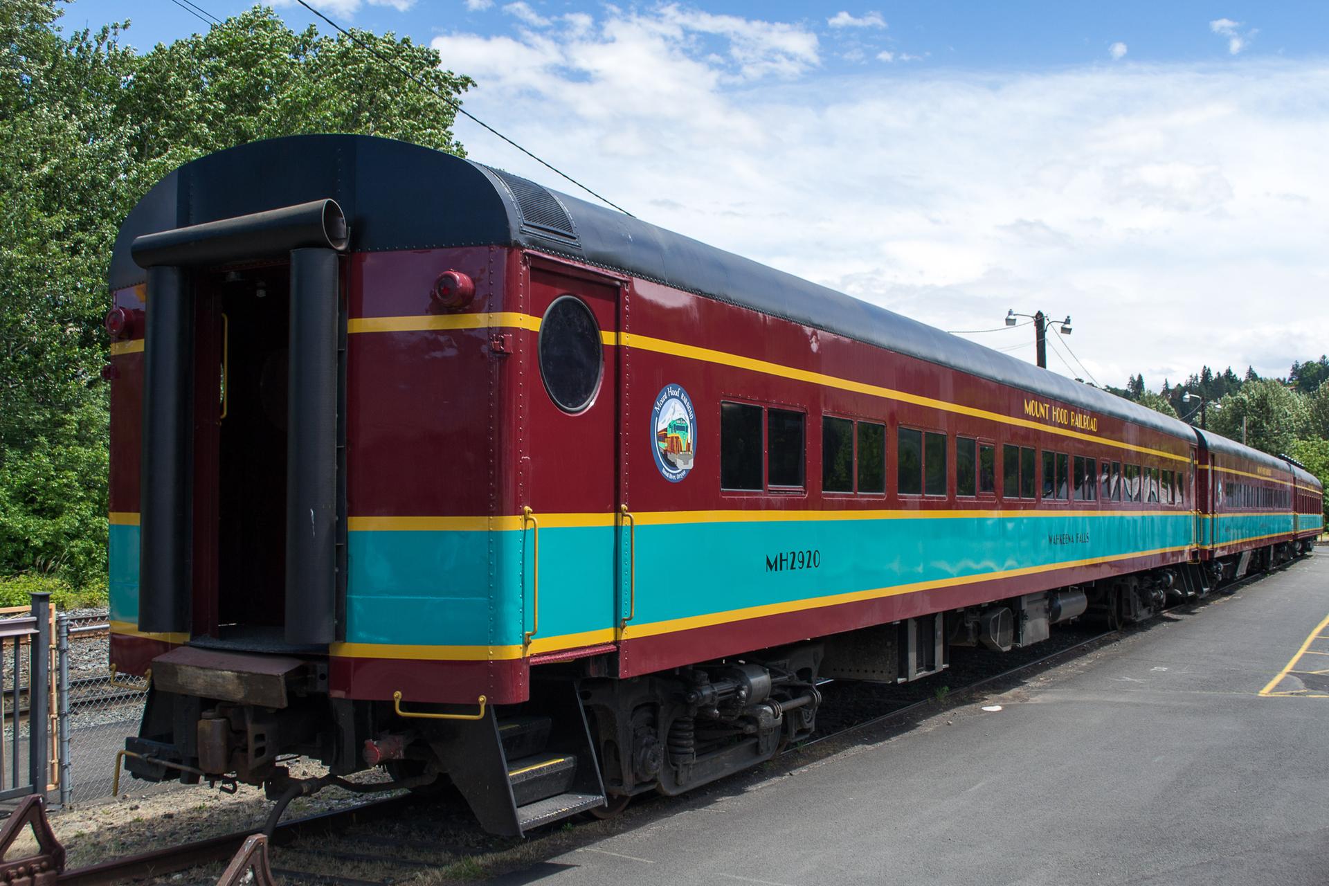 A colorful passenger train, red, blue, and yellow, parked on tracks outdoors.