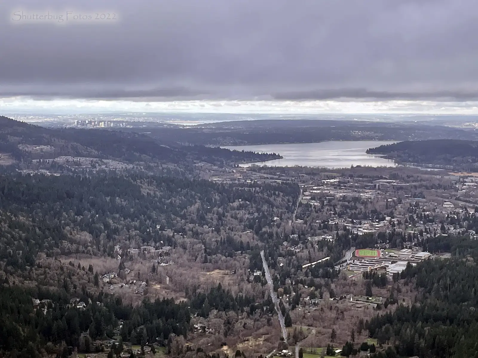 Overcast aerial view of a town, lake, and forested hills.