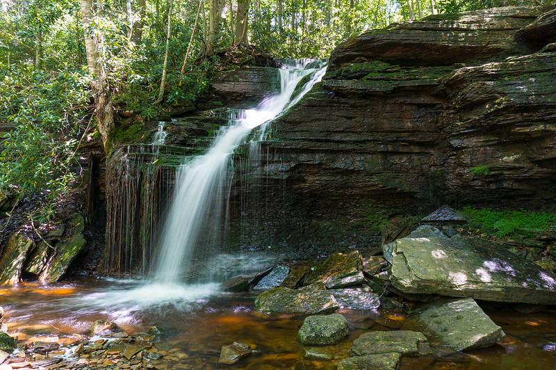 Waterfall plunging over dark rock formations into a shallow, rocky pool.