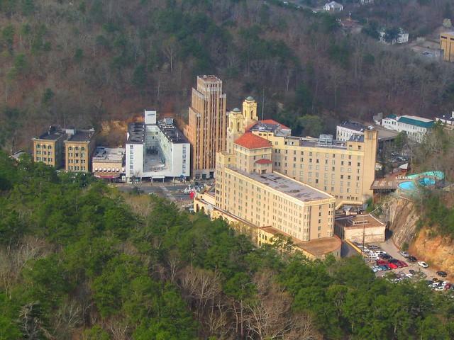 Aerial view of large buildings surrounded by forested hills under clear skies.