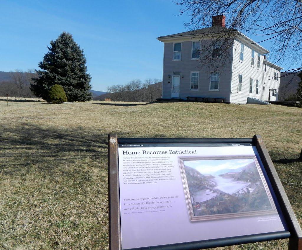 An information sign stands in a field before a white house and hills.
