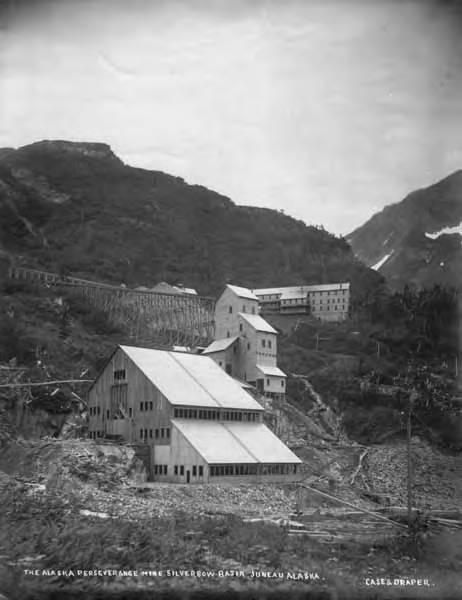 Black and white photo of old mining buildings nestled on a steep, rocky hillside.