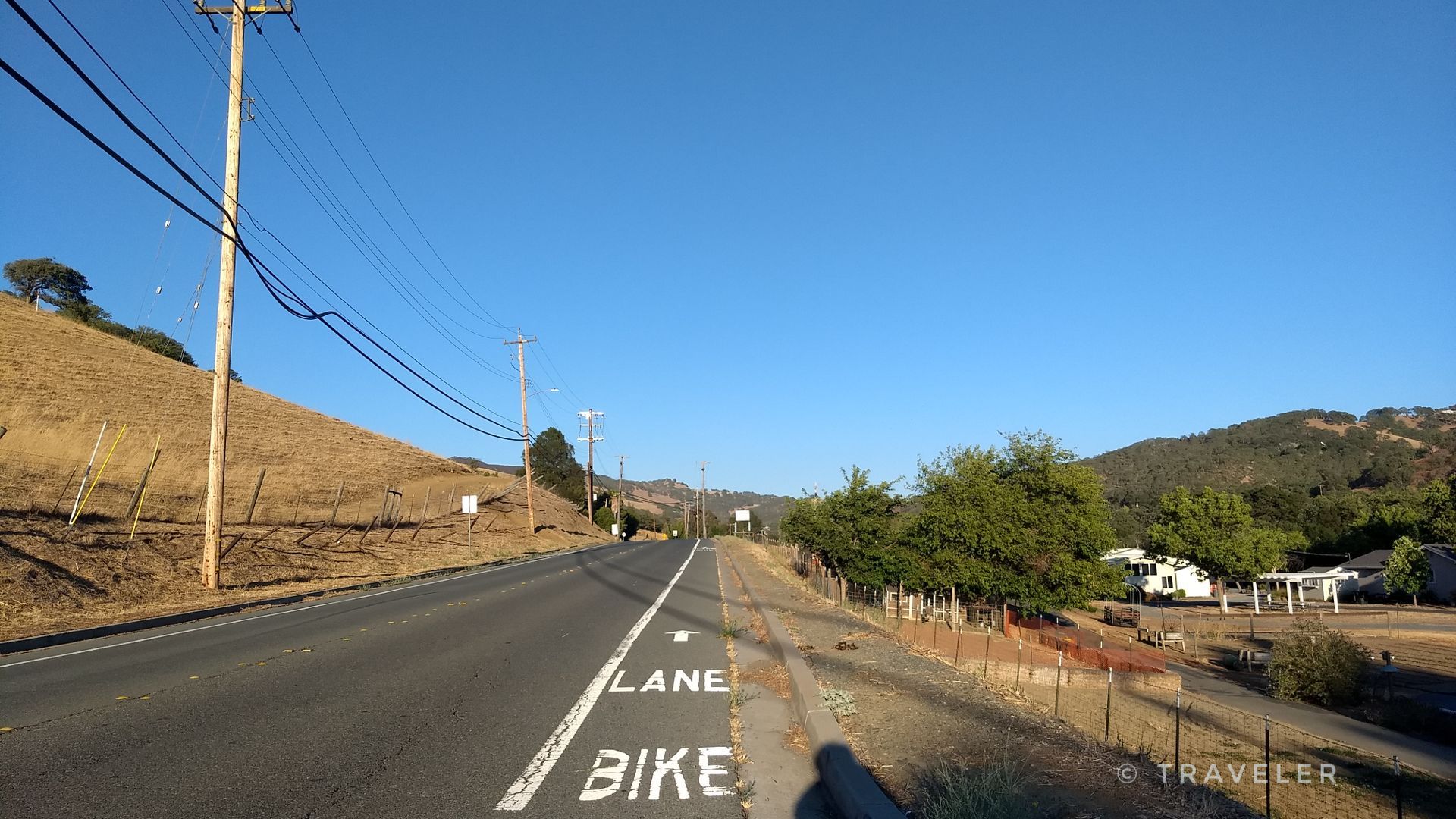 Road with a bike lane next to dry hills under a clear blue sky. - Clayton Ranch loop