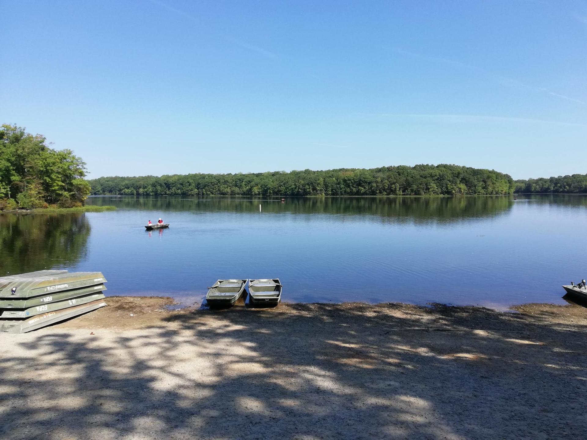 Sunny lake with a person in a small boat and empty boats on the shore.