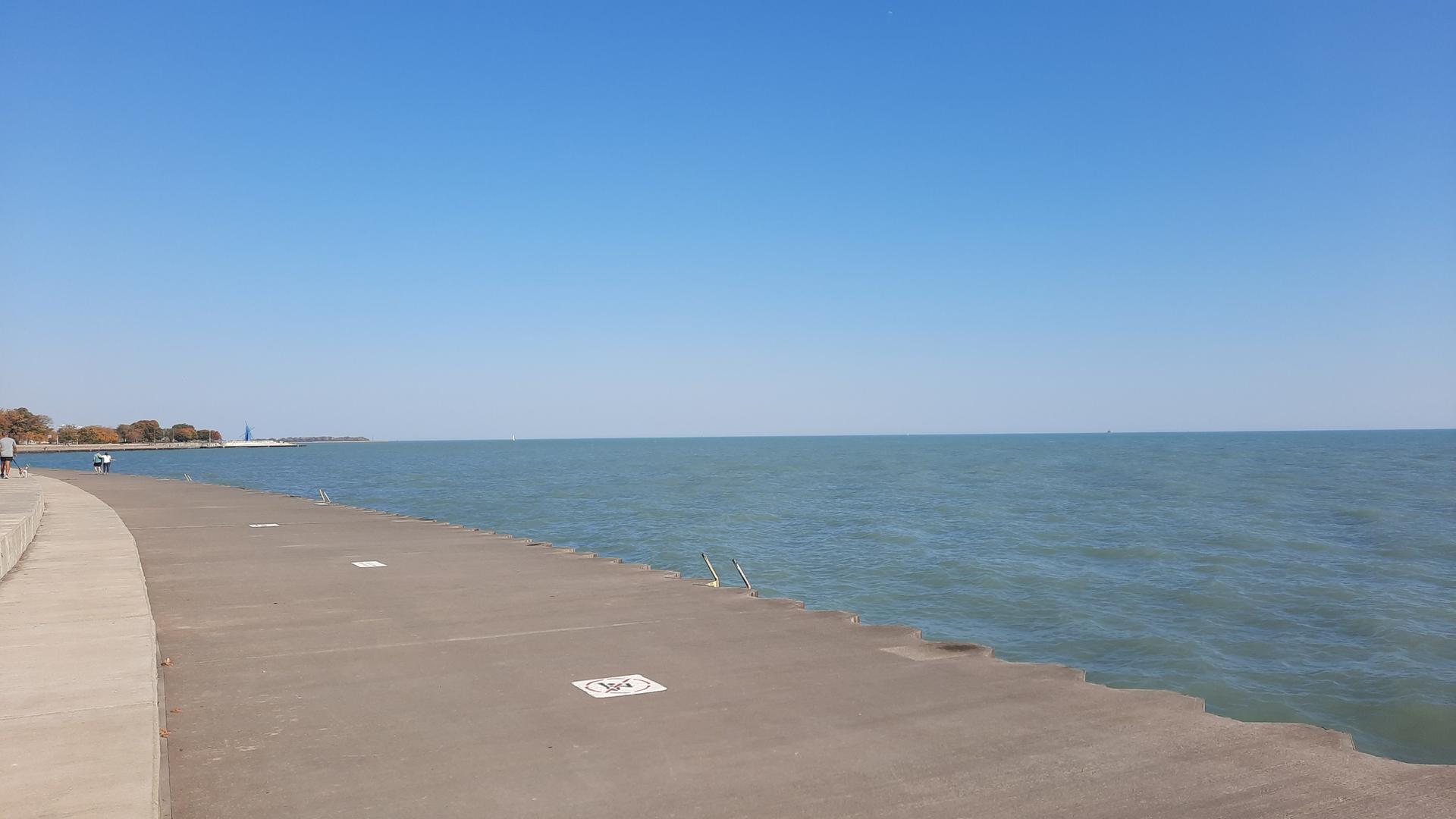Concrete pier extends into calm blue water under a clear sky.