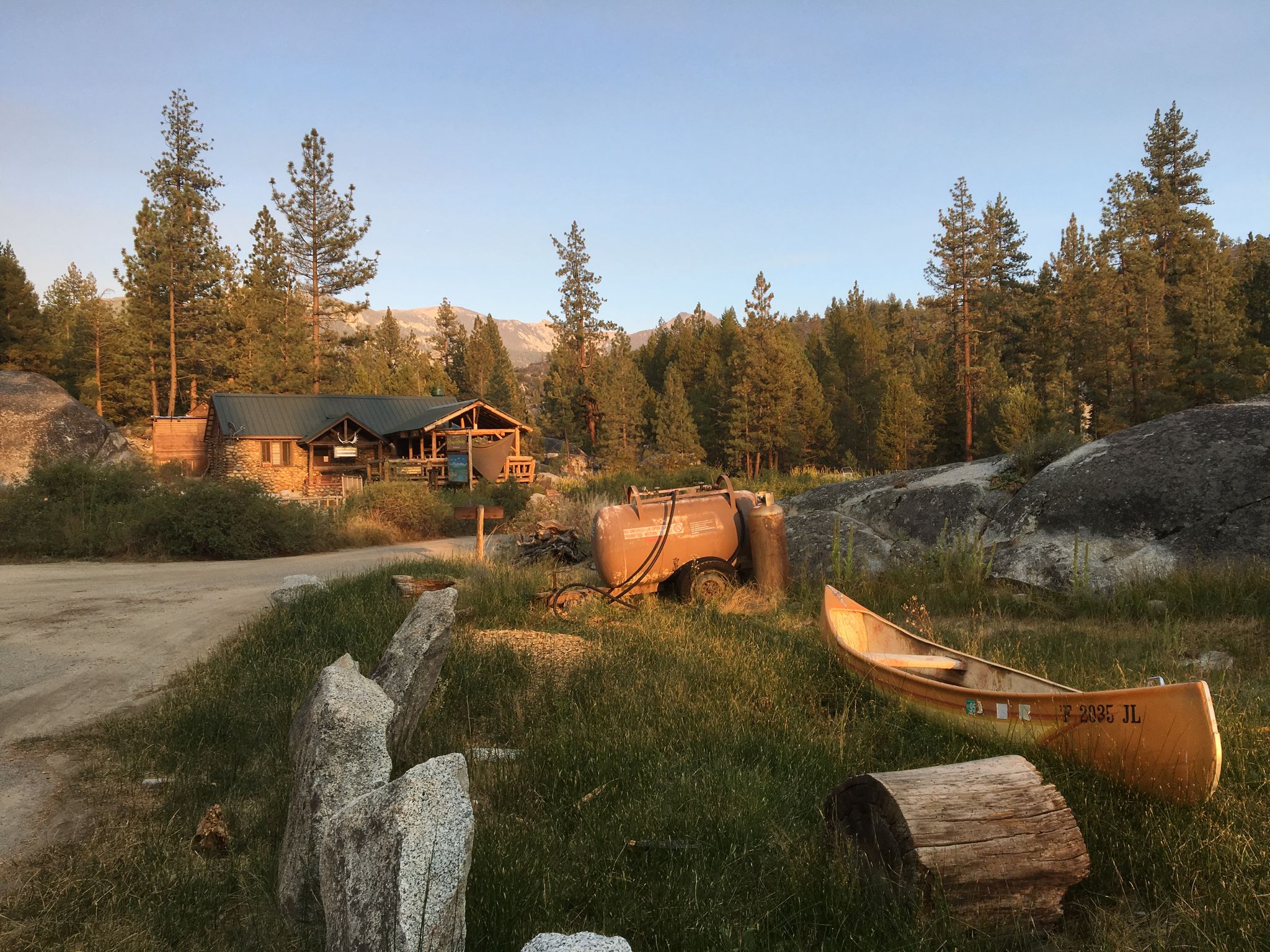 A rustic cabin and canoe in a sunlit forest clearing at golden hour. - Huntington Lake to Mono Hot Springs
