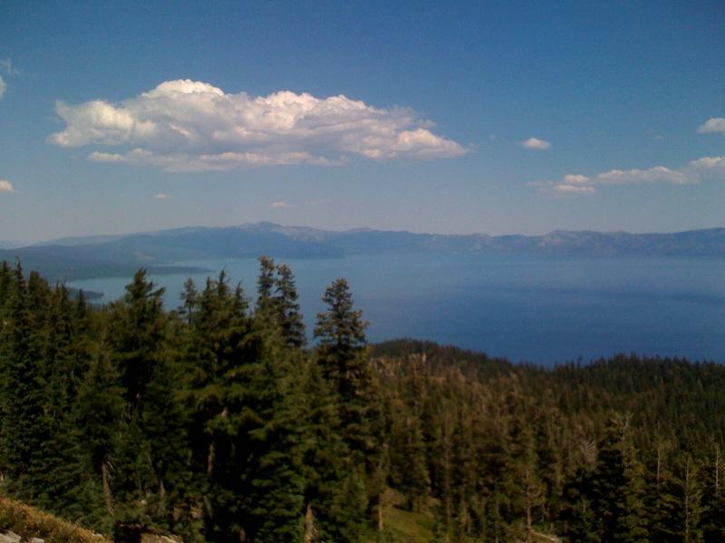 Panoramic view of a large blue lake surrounded by dense evergreen forests under a clear sky.