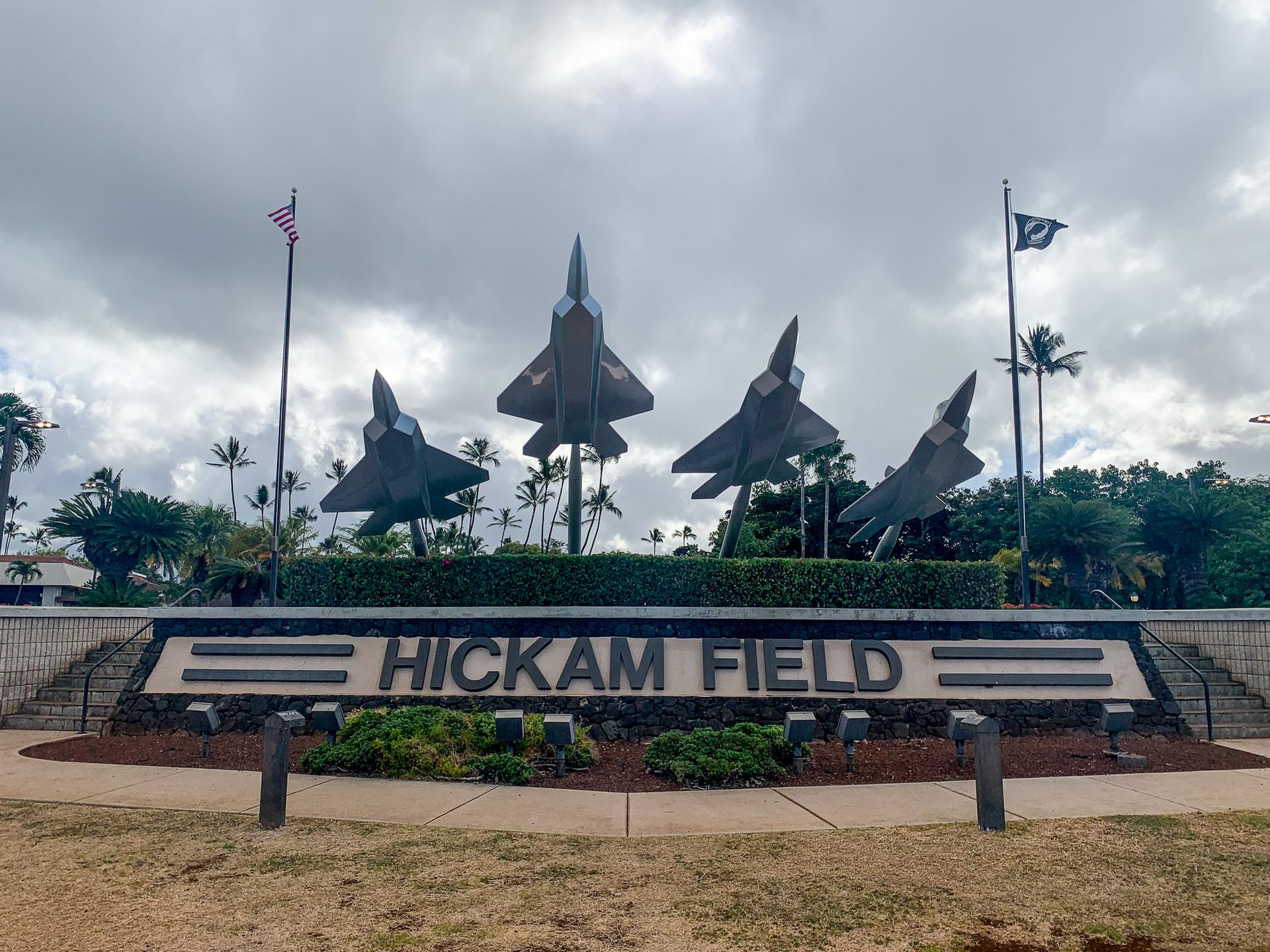 Four fighter jet models on a monument with palm trees under a cloudy sky.