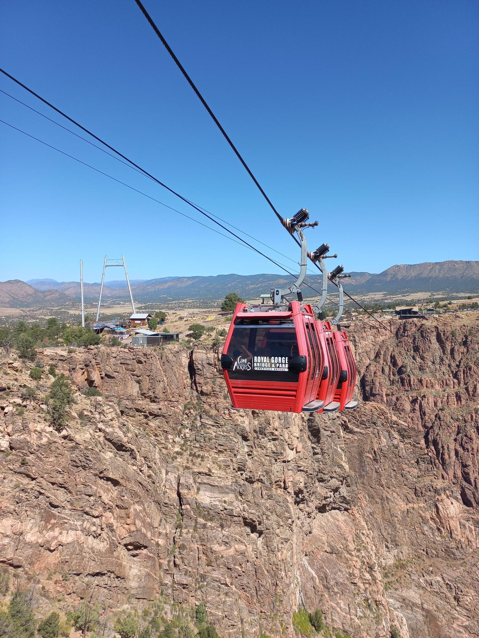 Red gondola cable car moving over a rocky canyon under a clear sky.