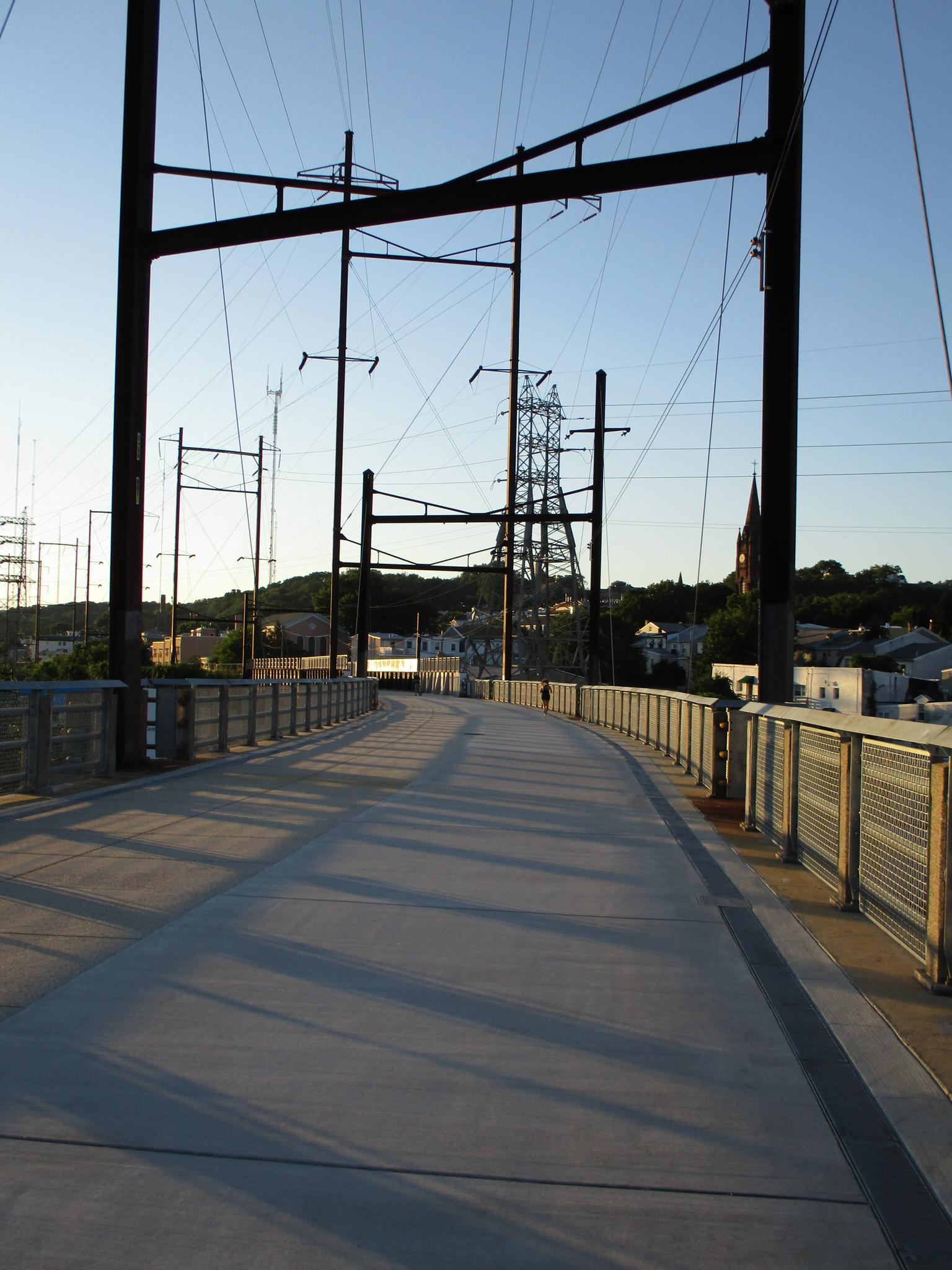 A concrete pedestrian path with power lines and long shadows under a clear sky.