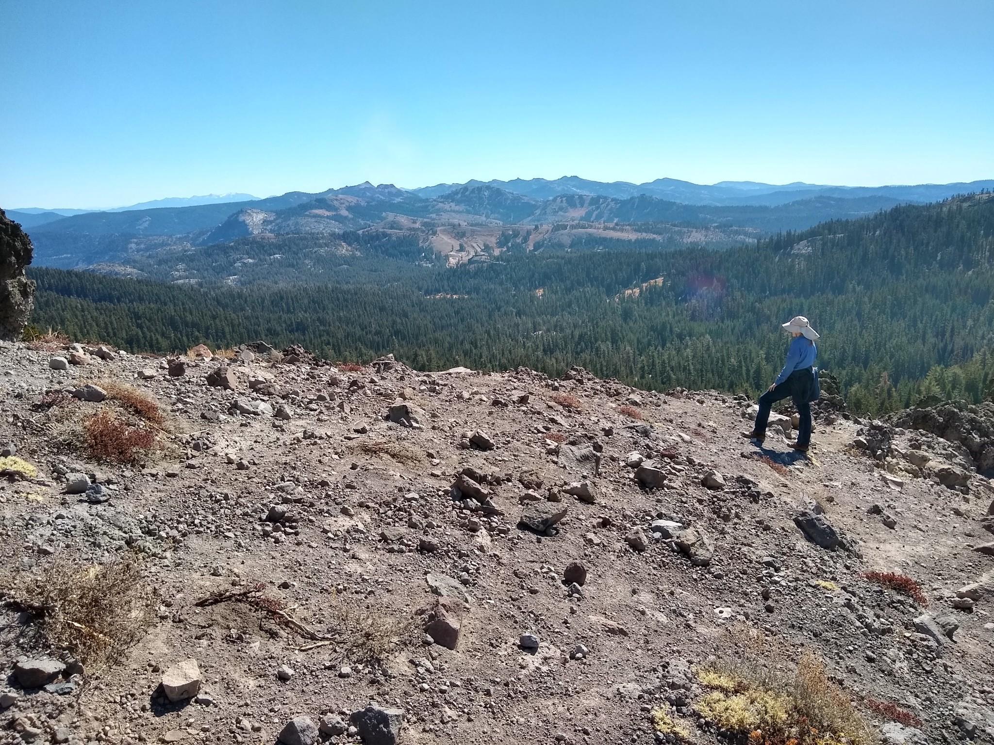 Person in a hat looking at a vast forested mountain landscape.