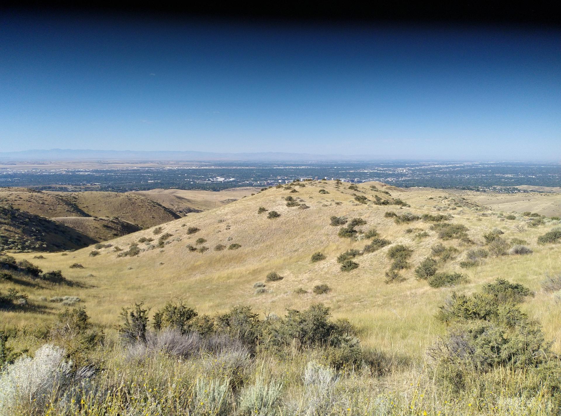 Rolling dry hills under a clear blue sky, with a distant city visible.