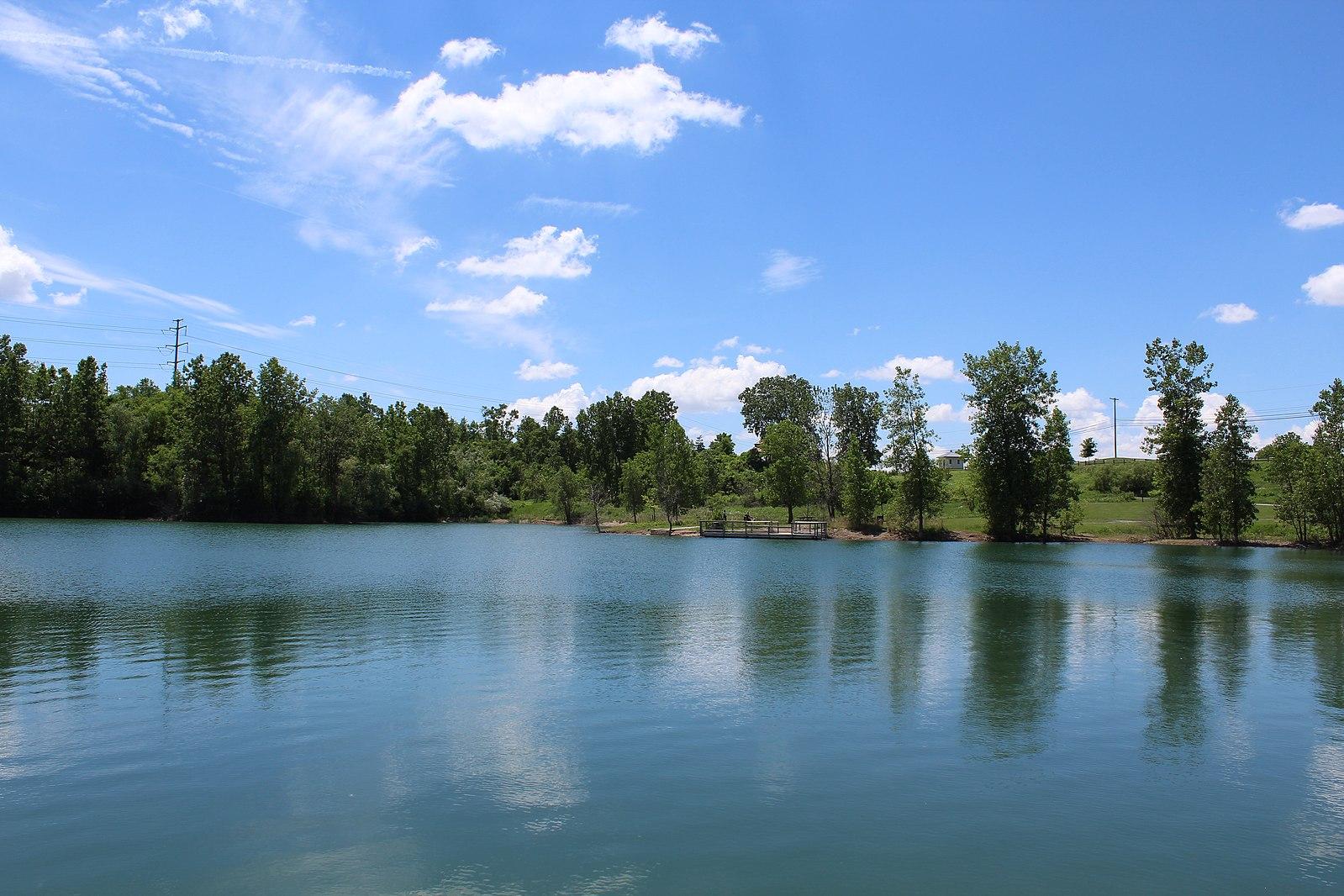 Bright sunny day over a calm lake bordered by lush green trees.