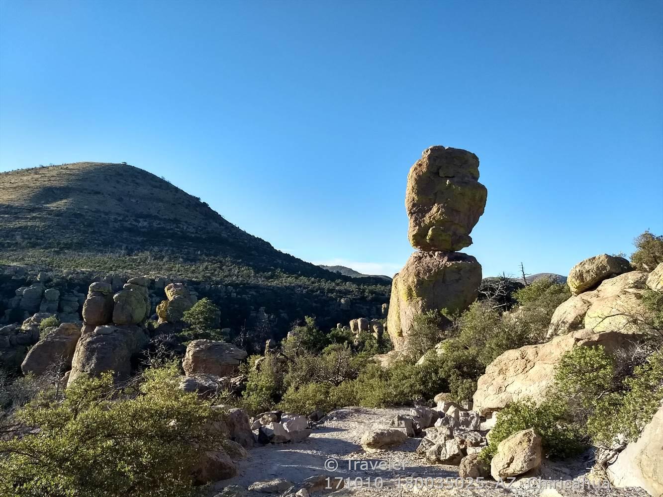 A large, balanced rock formation on a sunny day with distant hills.
