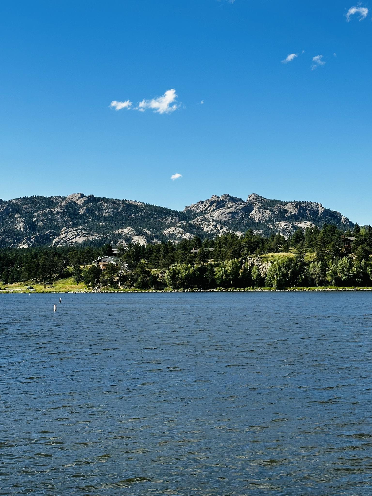 Blue lake with rocky, forested mountains under a bright, clear sky.
