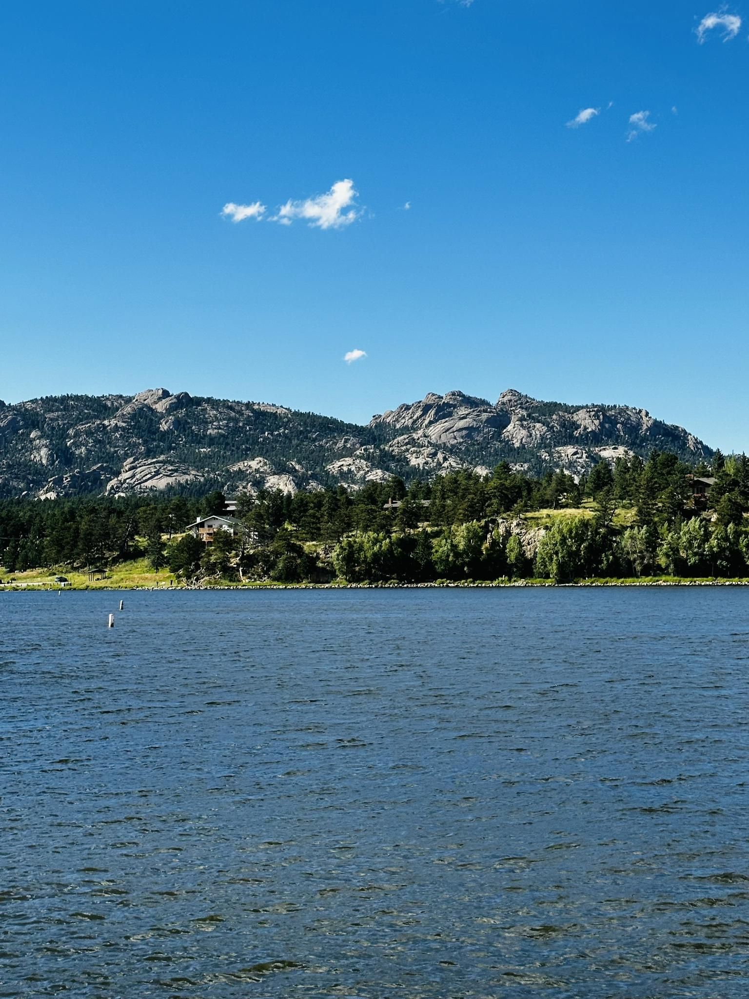 Blue lake with rocky, forested mountains under a bright, clear sky. - Lake Estes Trail
