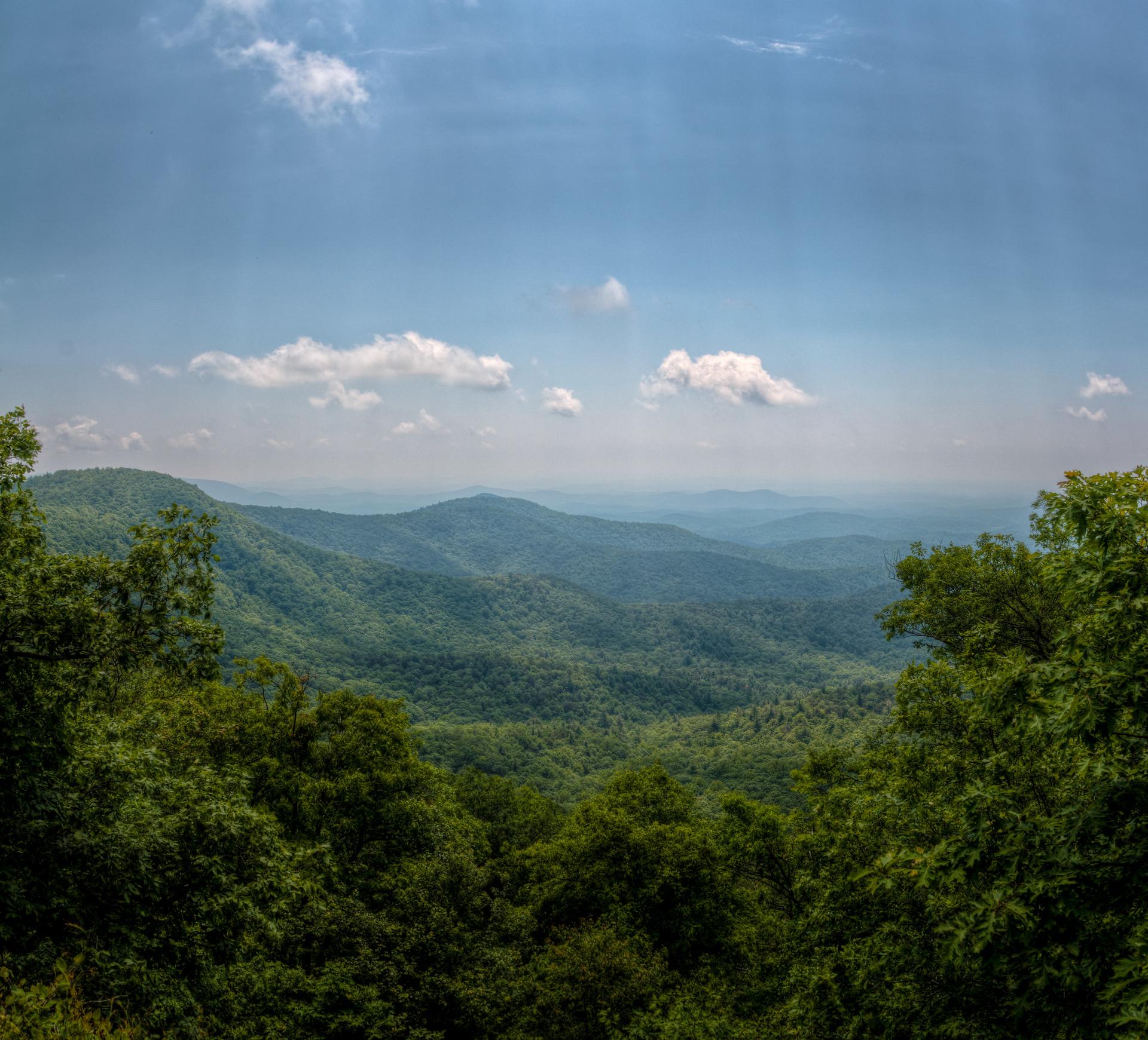 Vast green mountain ranges under a bright blue sky with scattered clouds.