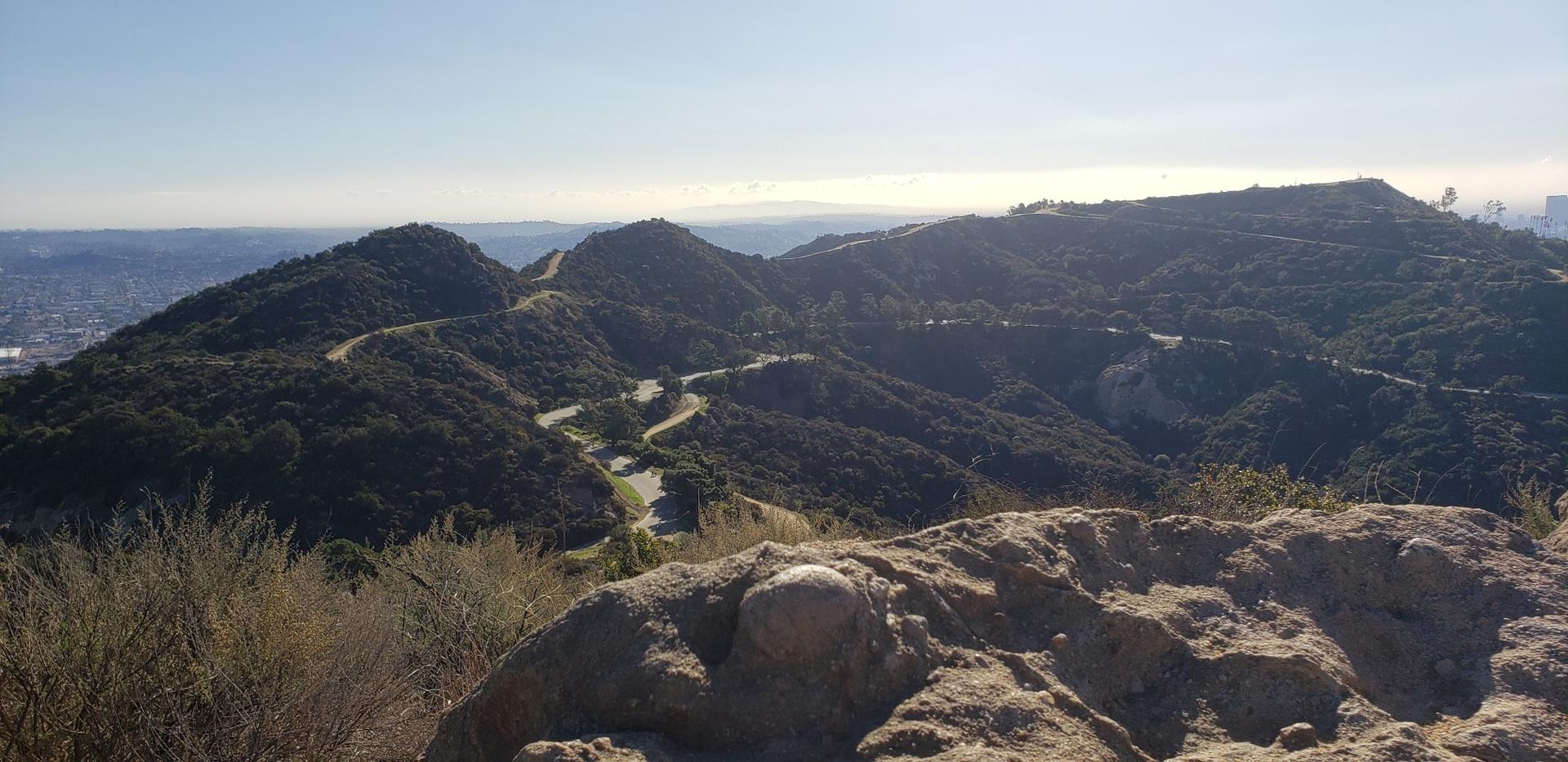 A panoramic view of green, rolling hills with winding roads under a clear sky.