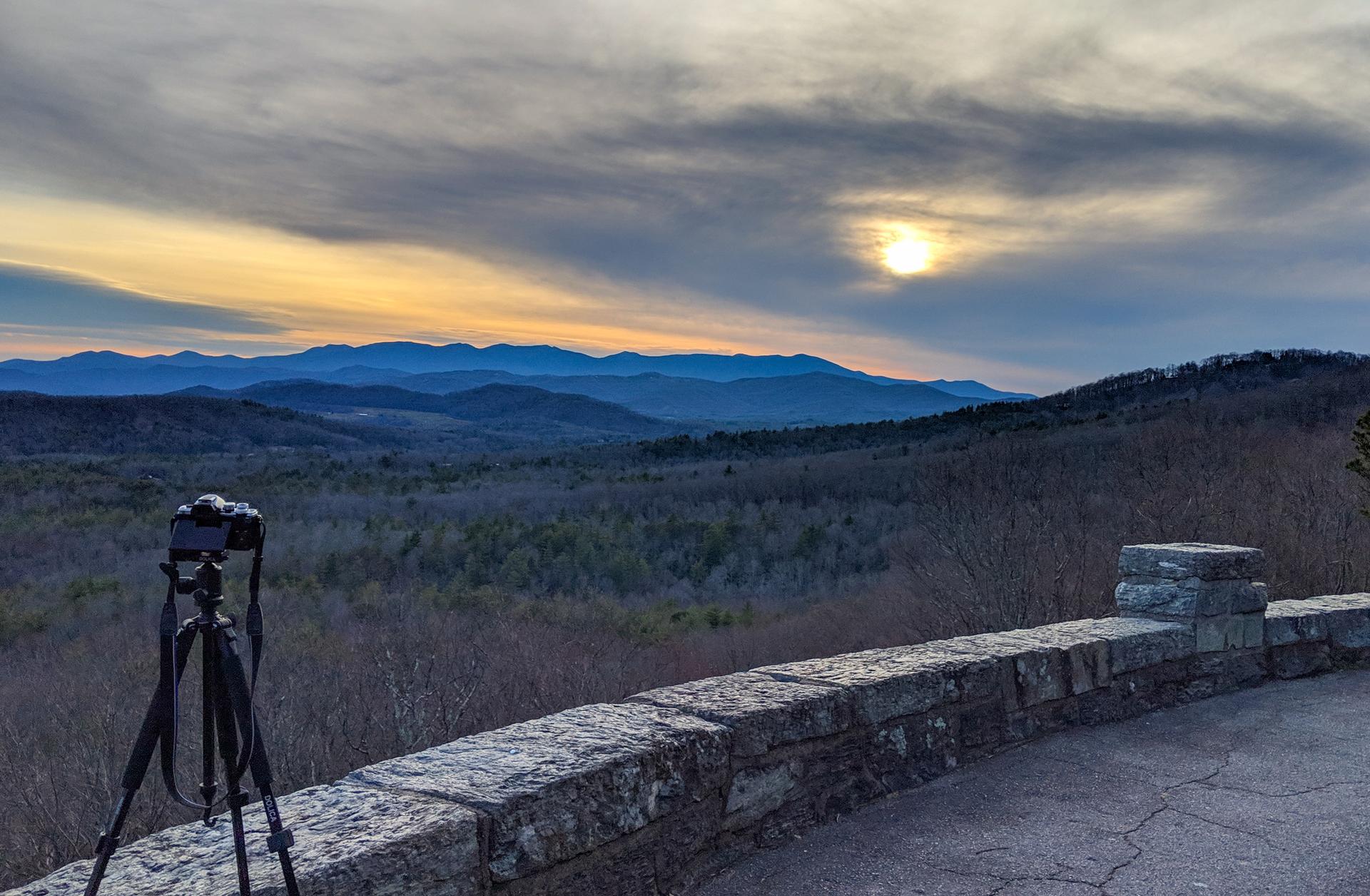 Camera on tripod overlooking a vast mountain range at sunset.