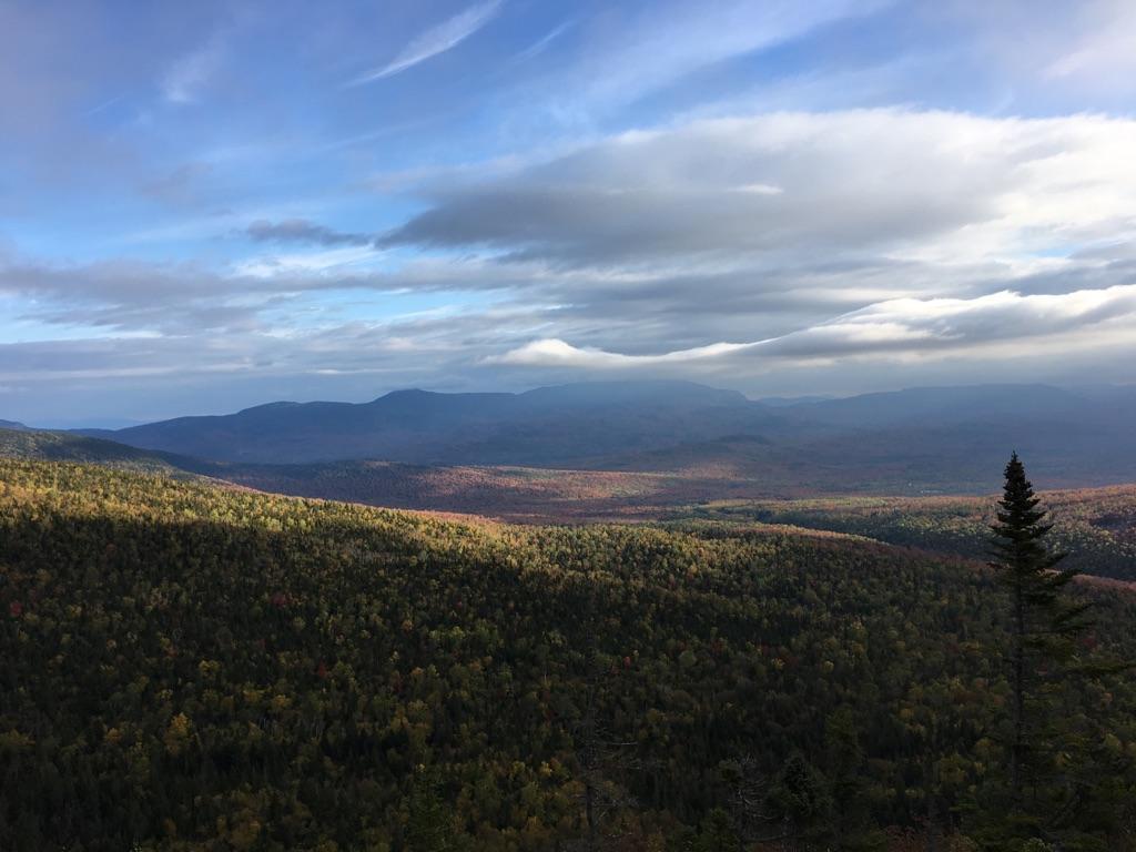 Autumn forest and mountains bathed in sunlight under a dramatic cloudy sky.