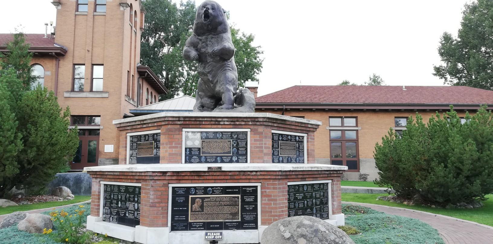 Large bear statue on a brick pedestal in front of a building.