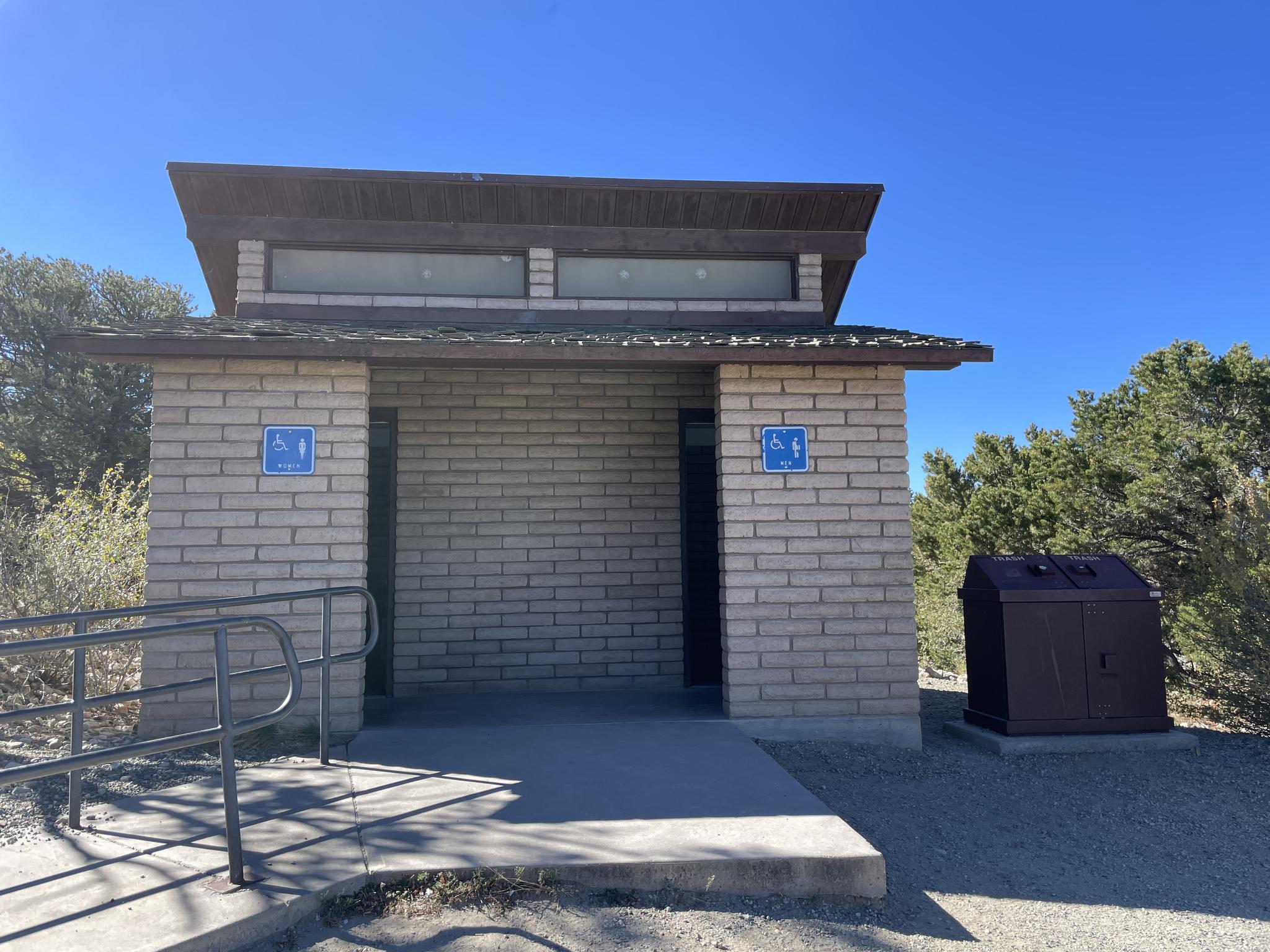 Brick restroom building with accessible ramps under a clear blue sky.