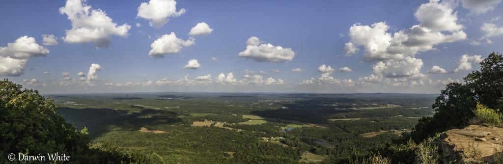 Panoramic view of a vast forested landscape under a bright, cloudy sky.
