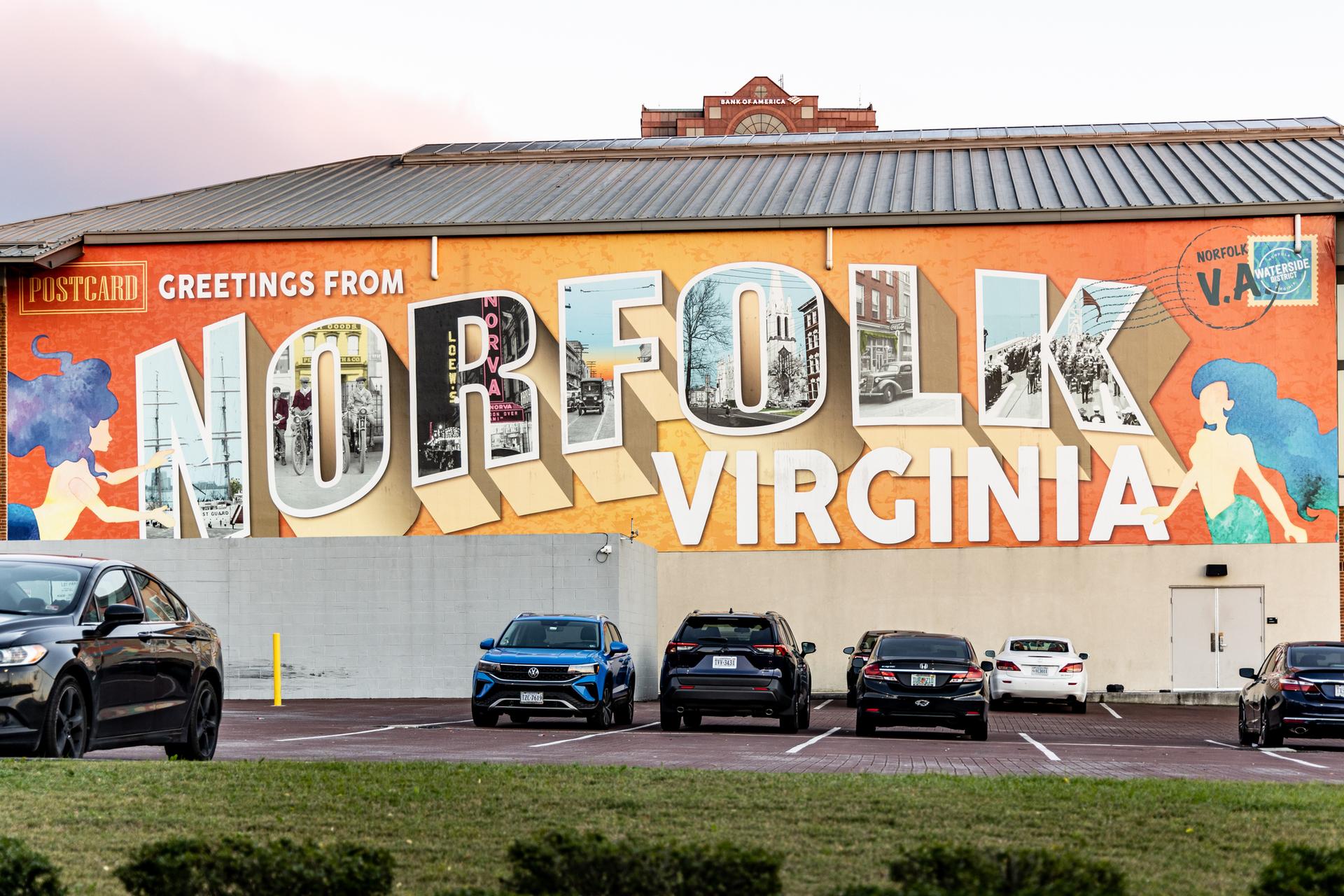 Building with a large, colorful postcard-style mural and parked cars.