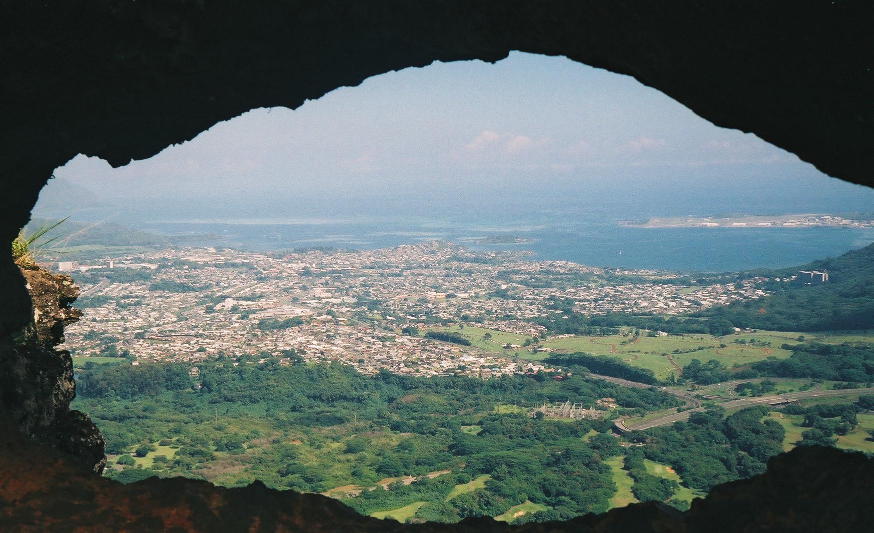 City and ocean viewed through a dark cave opening on a bright day.
