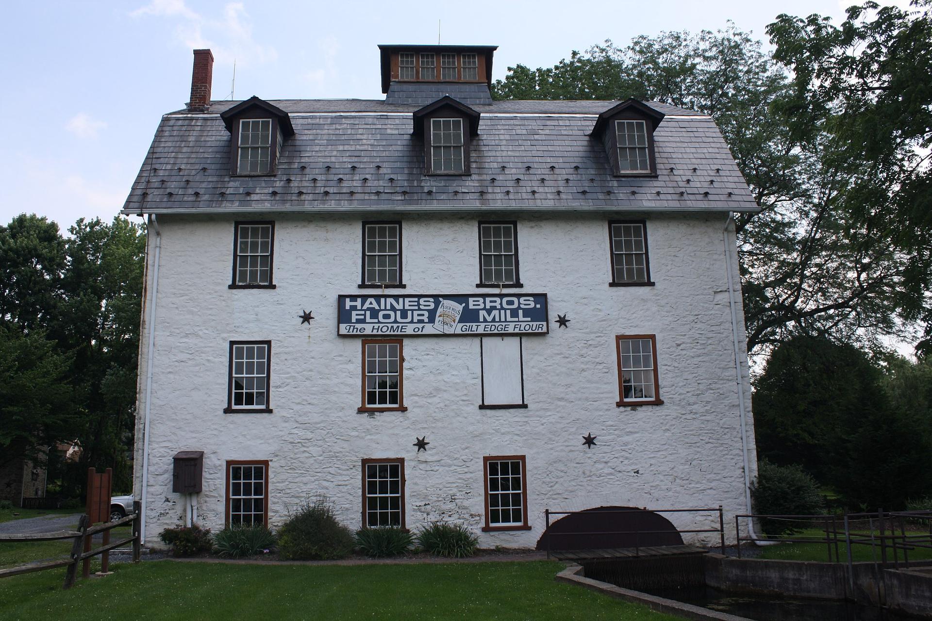 Historic white mill building with dark roof, green lawn, and surrounding trees.