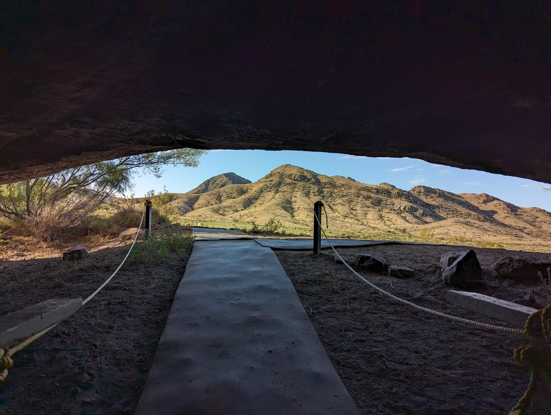 View from a dark cave opening showing a path leading to sunny desert mountains.