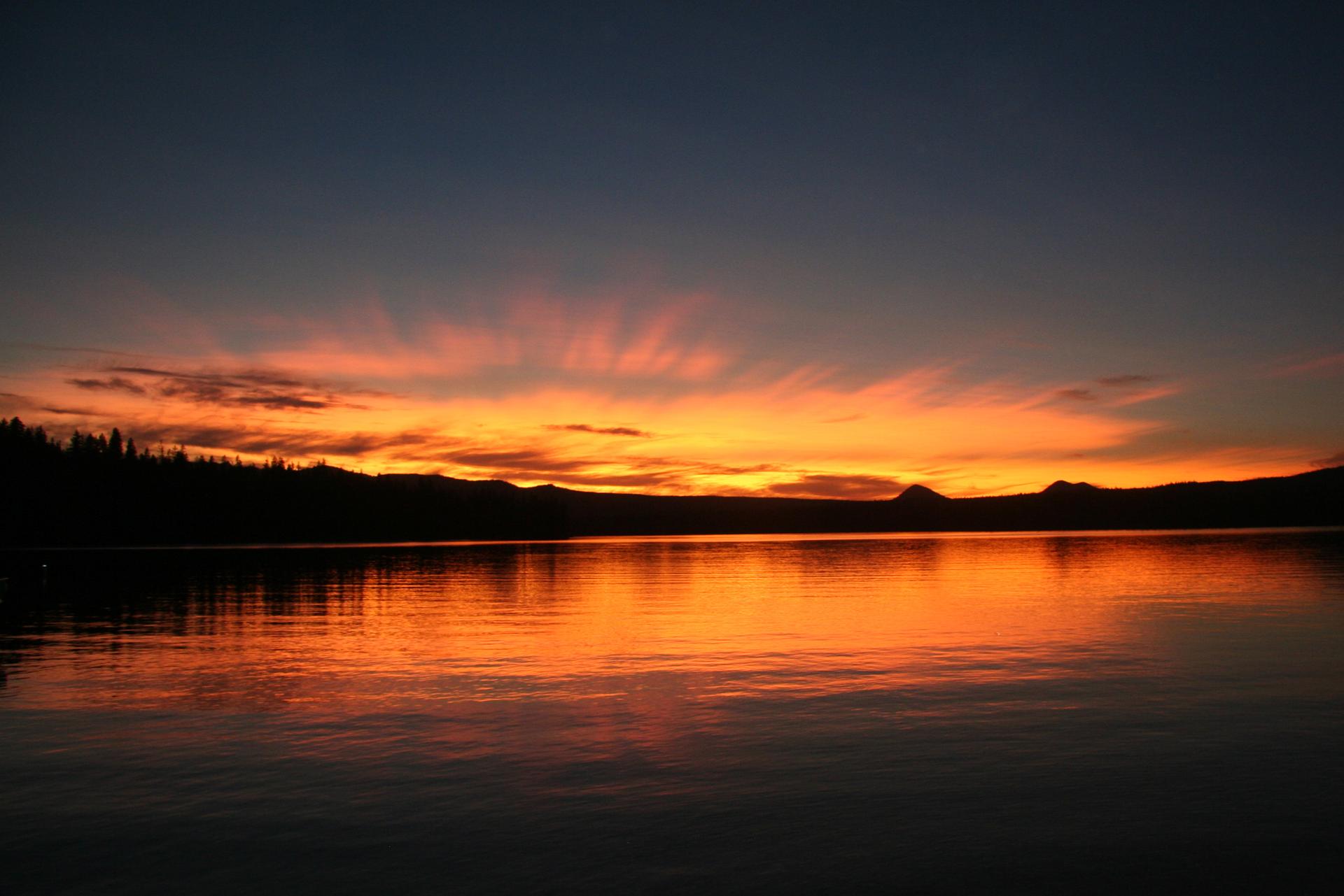 Vibrant orange and red sunset reflecting on a calm lake.