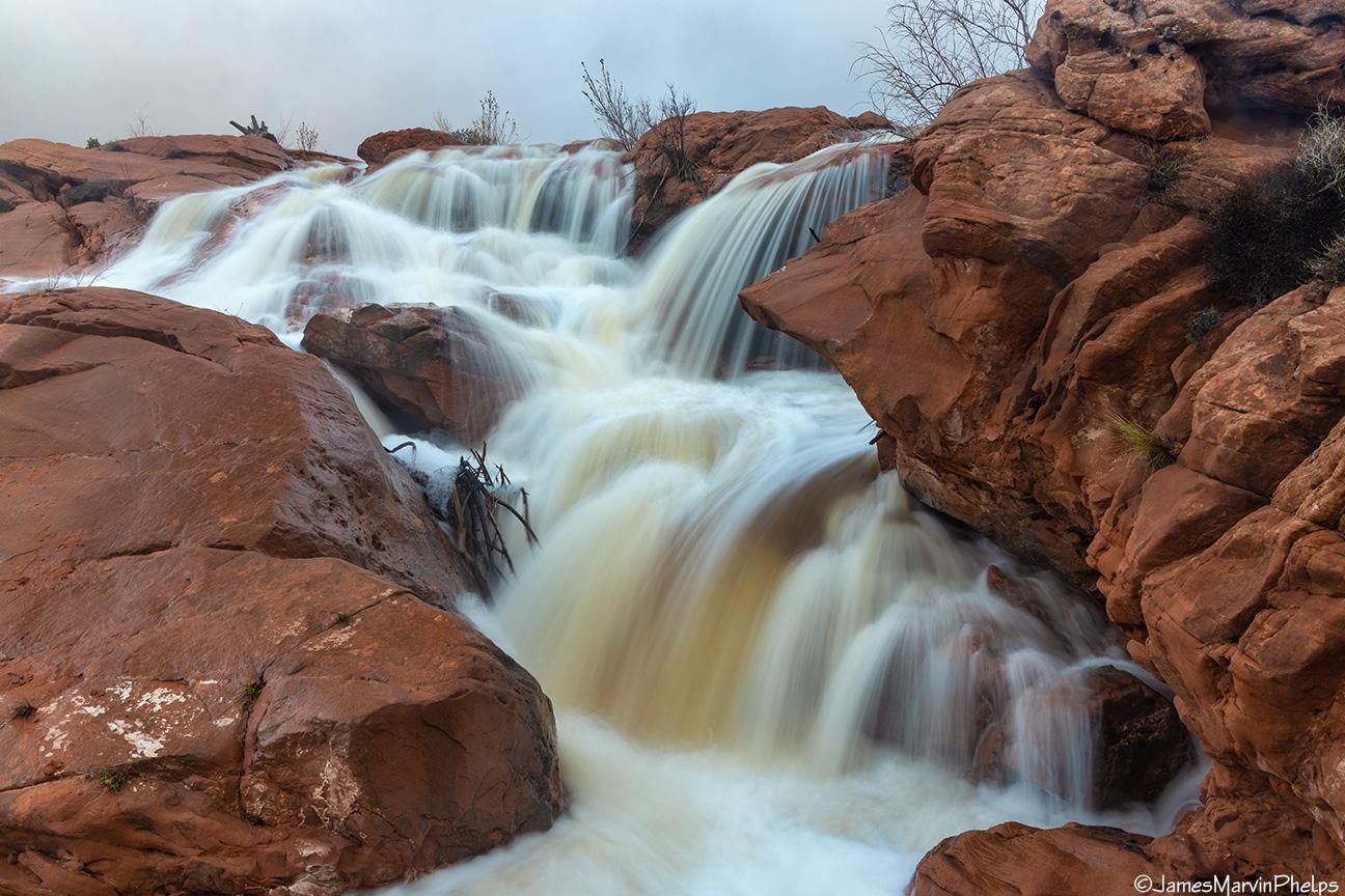 A powerful waterfall cascades over red rock formations with blurred, rushing water.