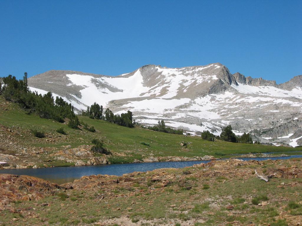 Bright day over snow-capped mountains, a blue lake, and green slopes.