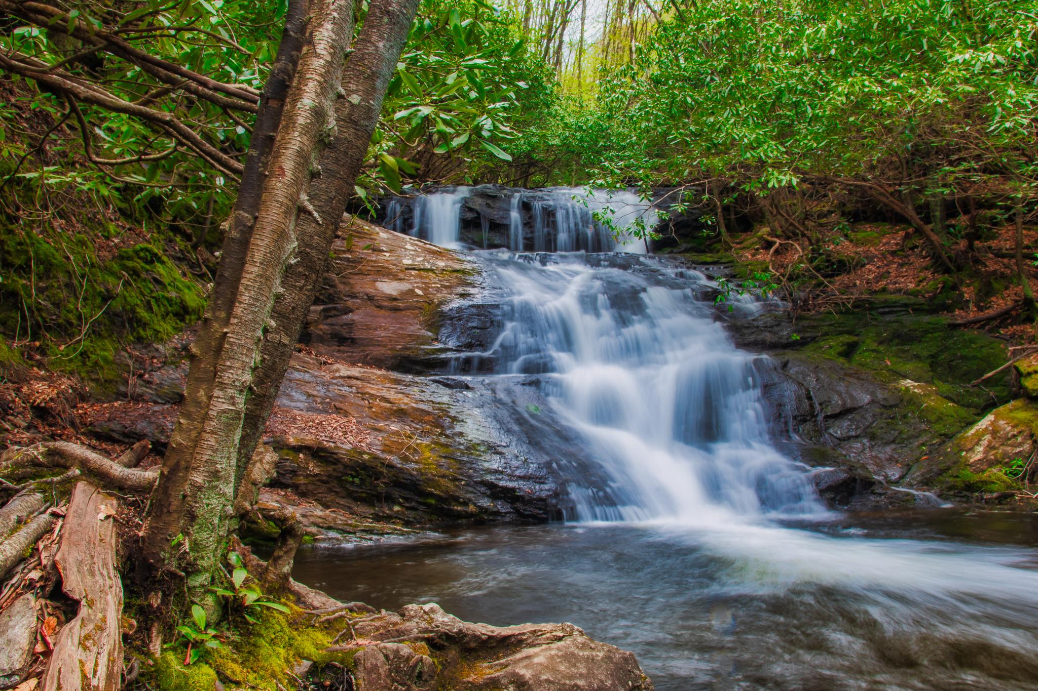 A multi-tiered waterfall cascades over mossy rocks in a lush green forest.
