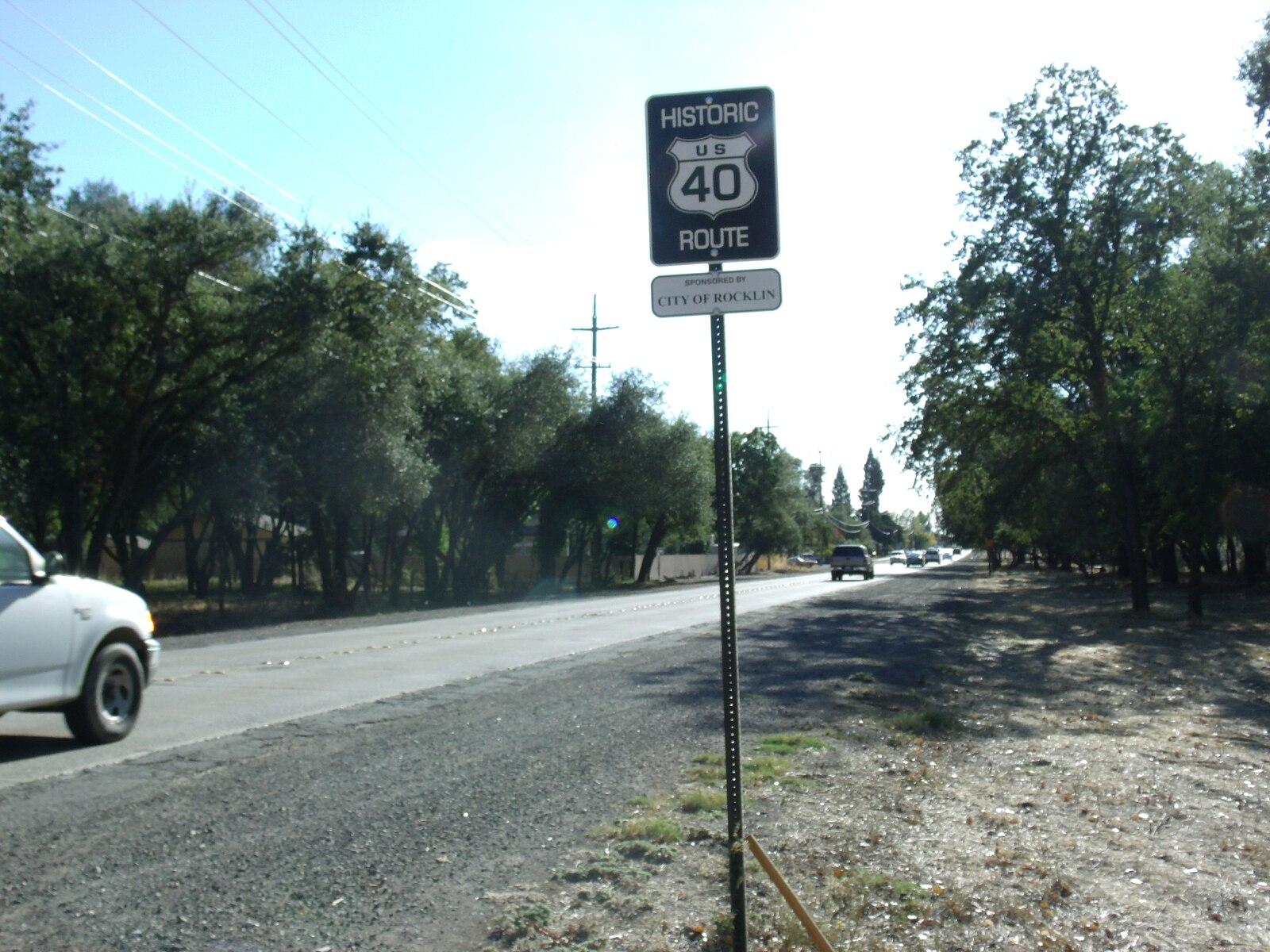 Roadside view with a historic route sign, trees, and a car driving.