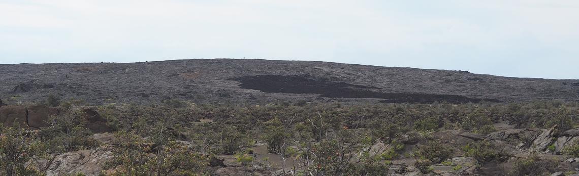 Expansive, barren volcanic landscape with a dark patch under a bright sky.