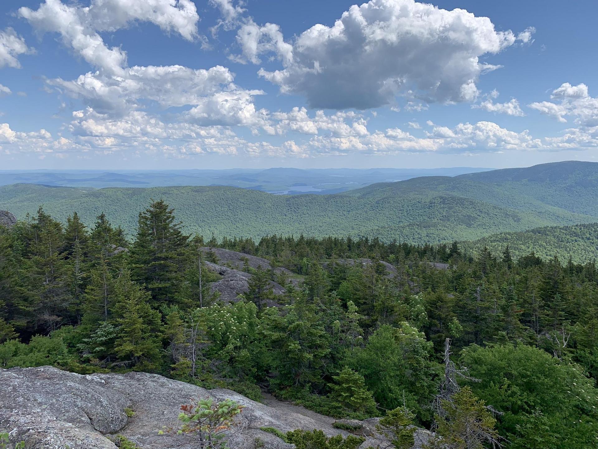 Expansive view of green forested mountains under a bright, cloudy sky.