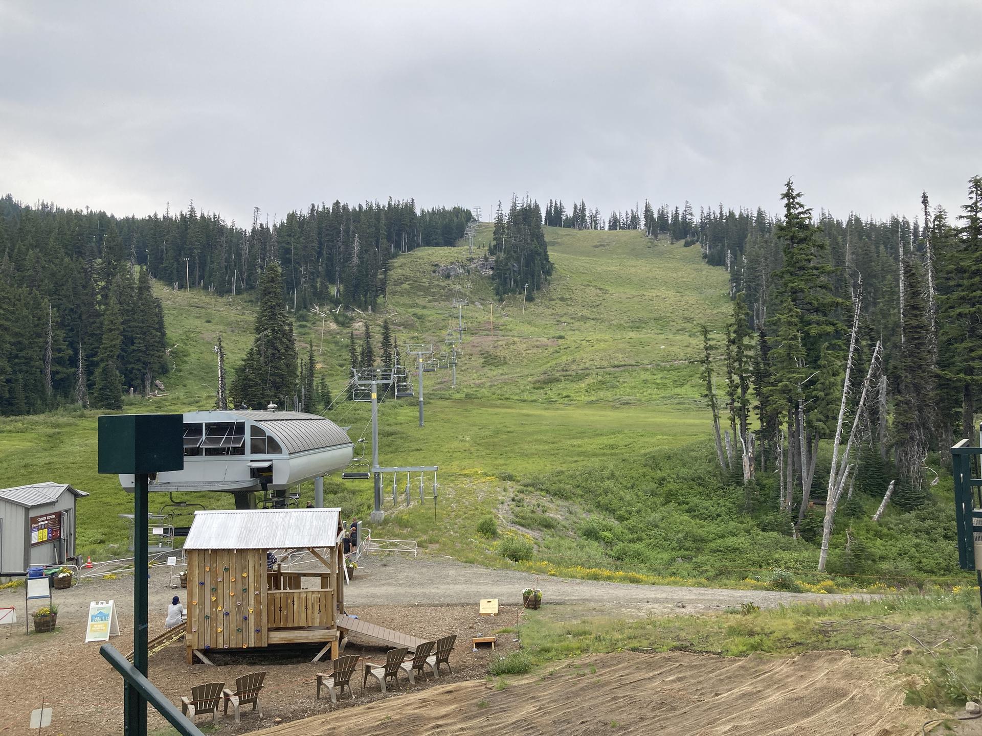 A ski lift overlooks a green, treeless mountain slope under a cloudy sky.