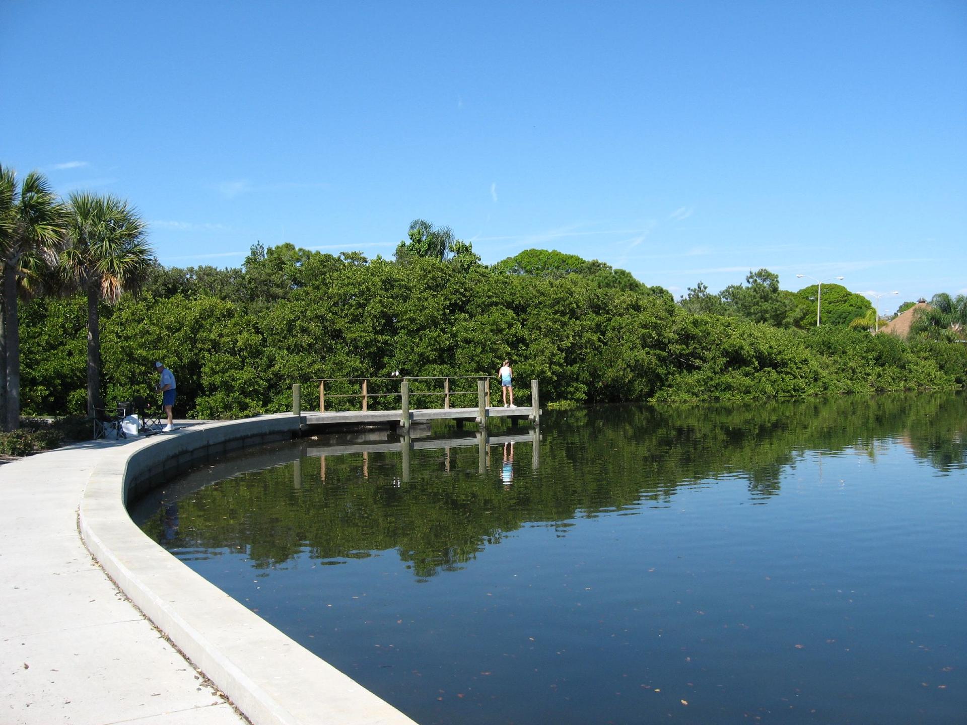 People on a wooden dock next to a curved path and calm water.