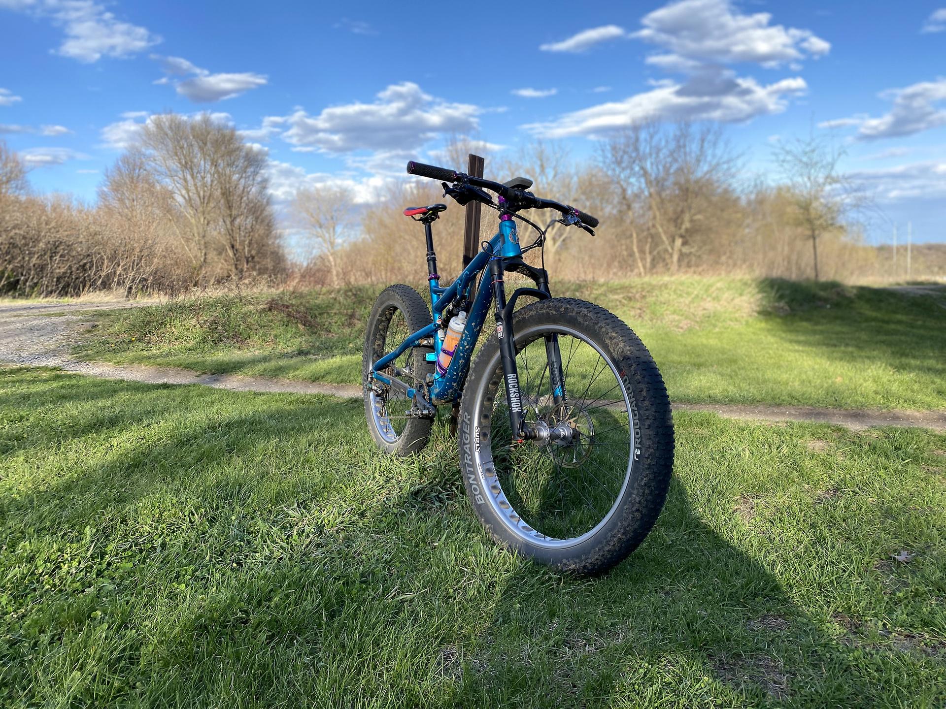 A blue fat-tire mountain bike rests on green grass under a bright blue sky.