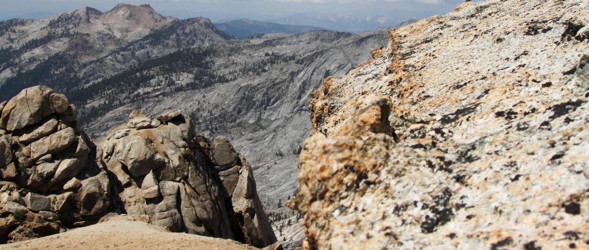 Close-up of rugged rocks with distant, barren mountains under a bright sky.
