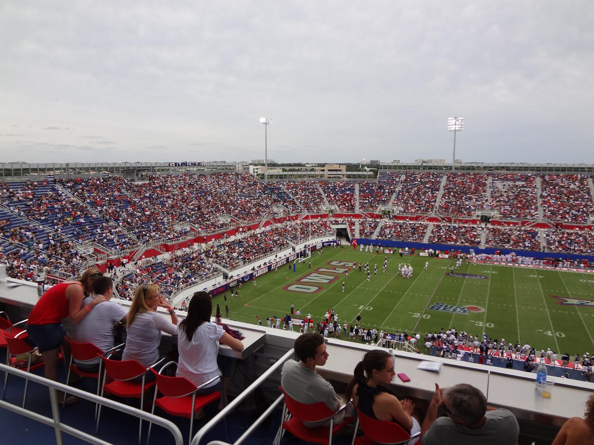 People watch a football game in a crowded stadium under an overcast sky.